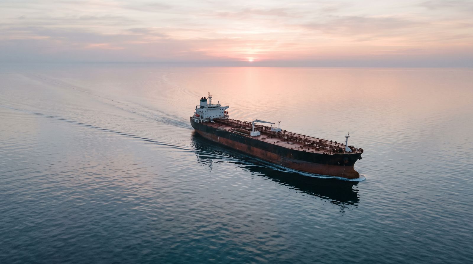 A large crude oil tanker on calm open water at dawn under a wide empty sky